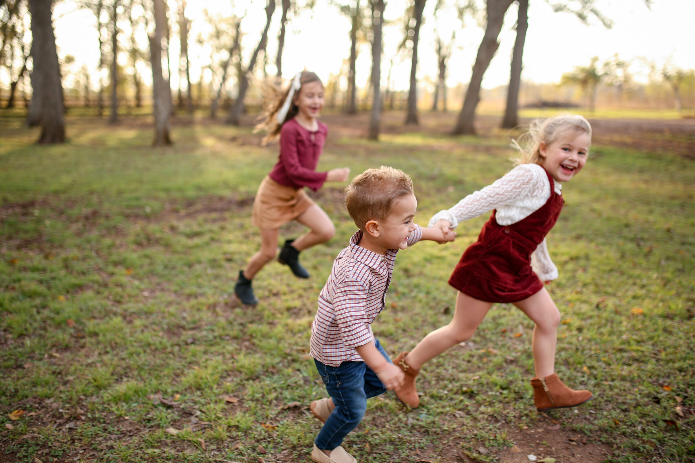Three siblings running and laughing through a grassy clearing during a fall mini session near Richmond, Texas