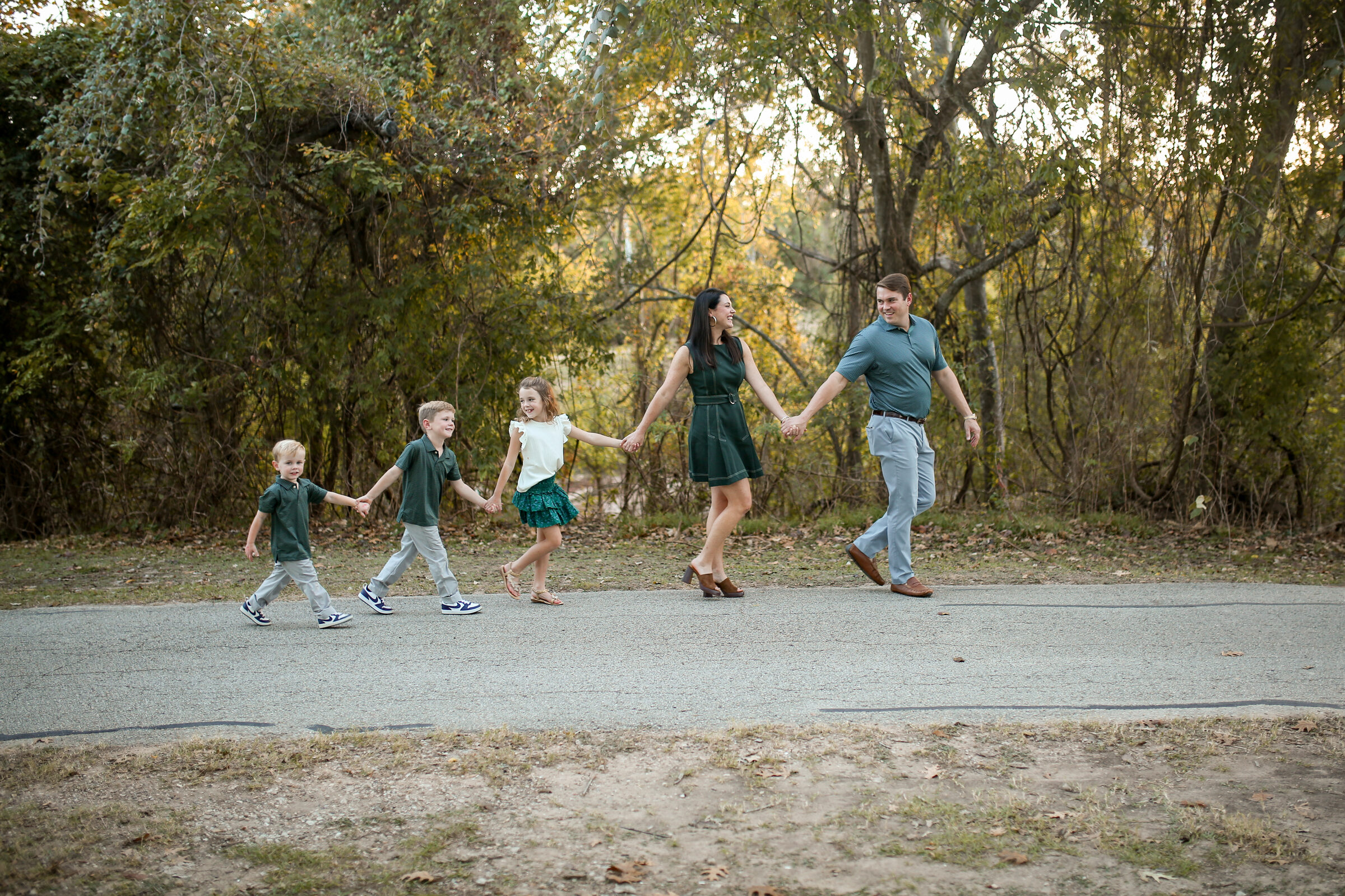 A family of five walking hand in hand along a wooded path at golden hour in Richmond, Texas