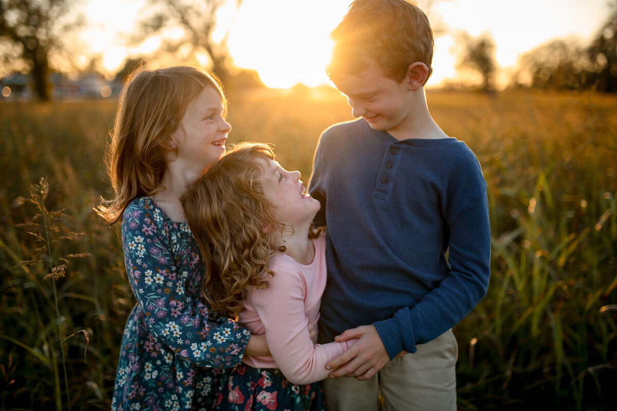 Three siblings hugging and giggling at sunset