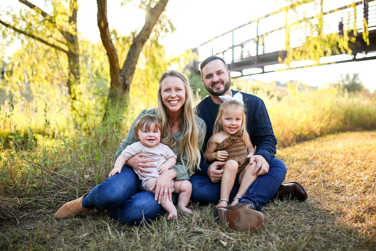 A young family of four snuggled together beneath a tree in golden light