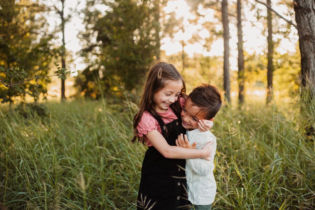 Two young siblings hugging in tall golden grass