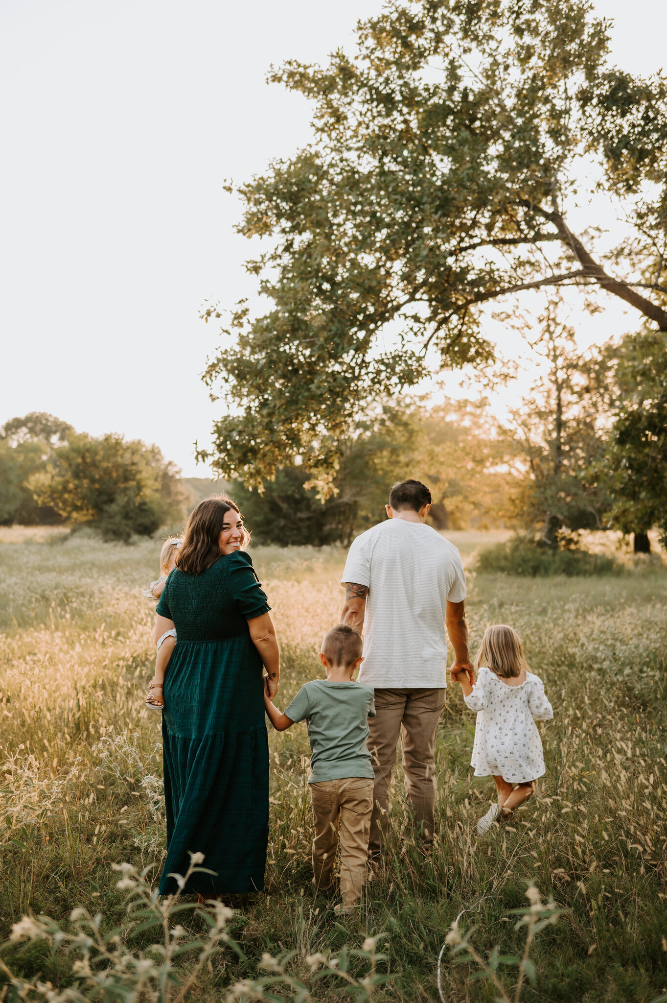 Nicole Whetzel, Richmond Texas family photographer, walking through a golden field with her family