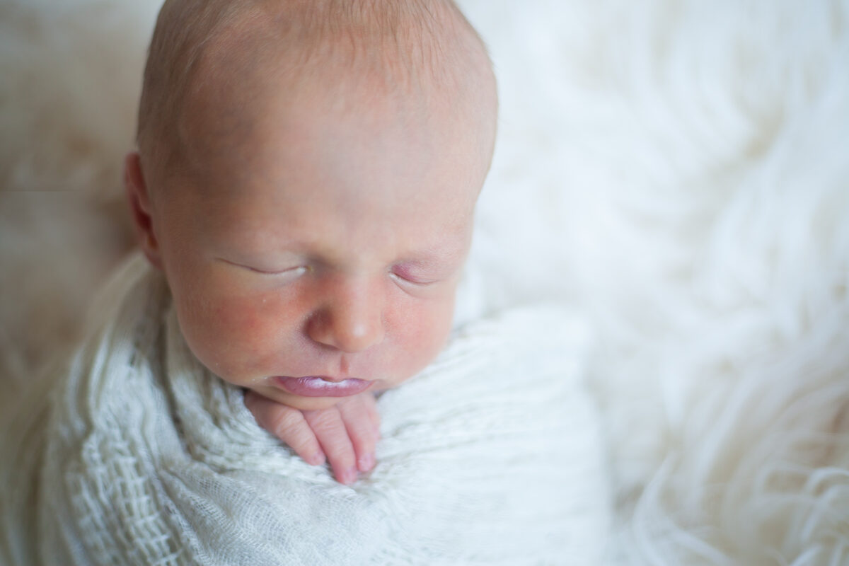 A soft-focus close-up of a newborn resting in cream knits