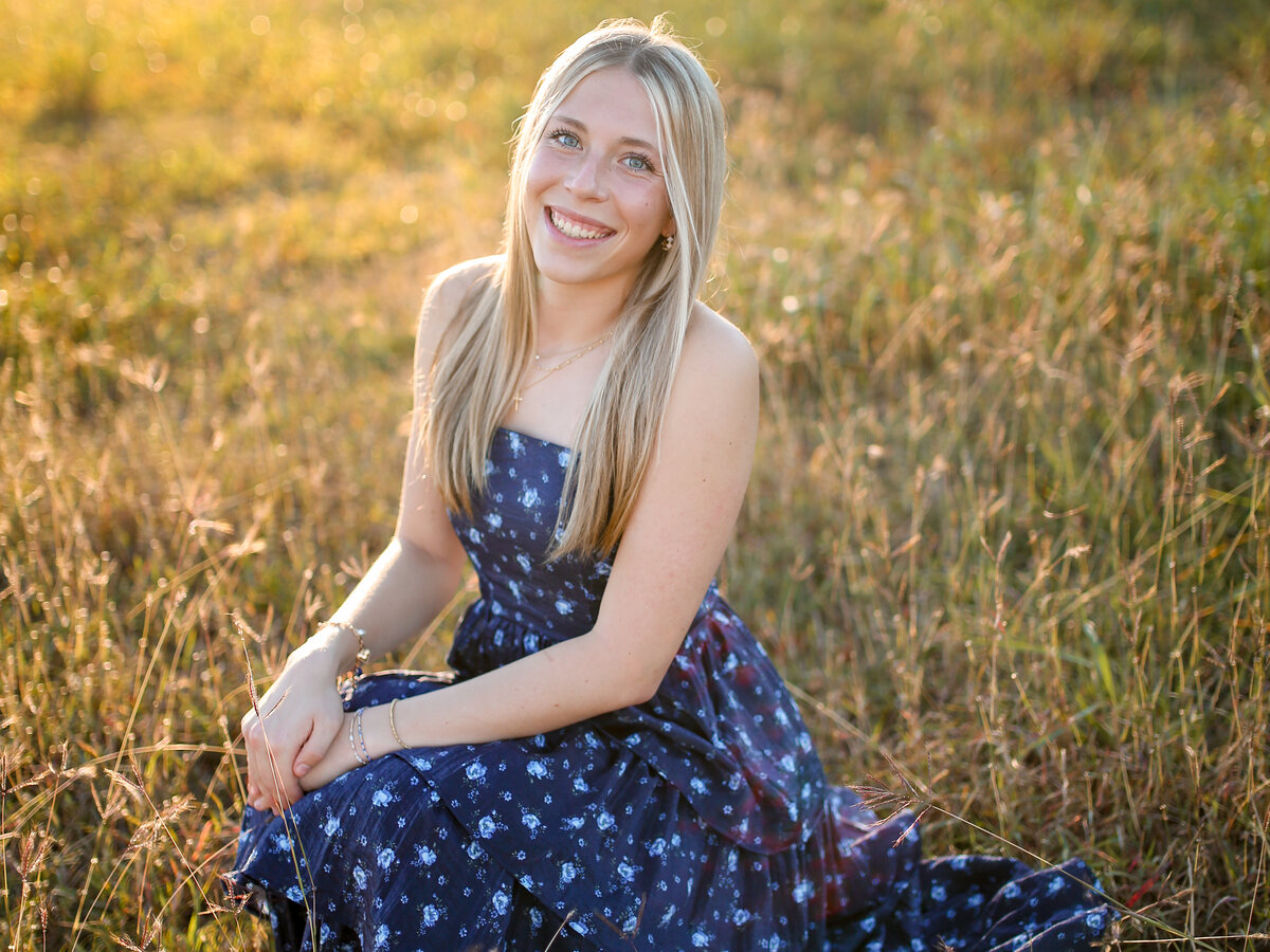 Eden sitting in a golden field in her navy floral dress