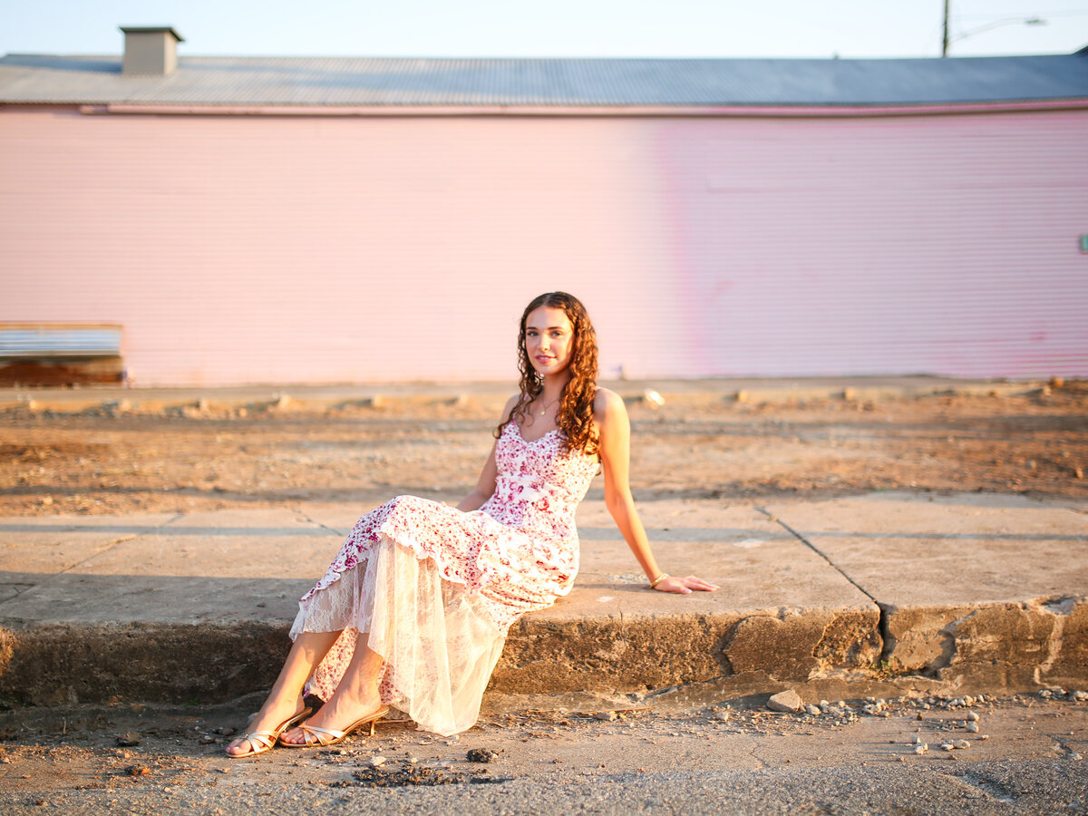 Madi in a pink lace dress on the curb by the pink wall
