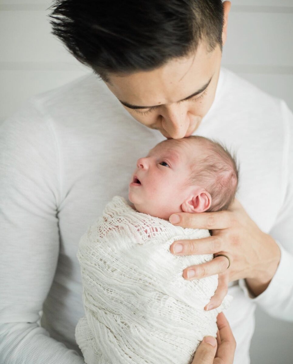 A father kissing his newborn wrapped in cream knit