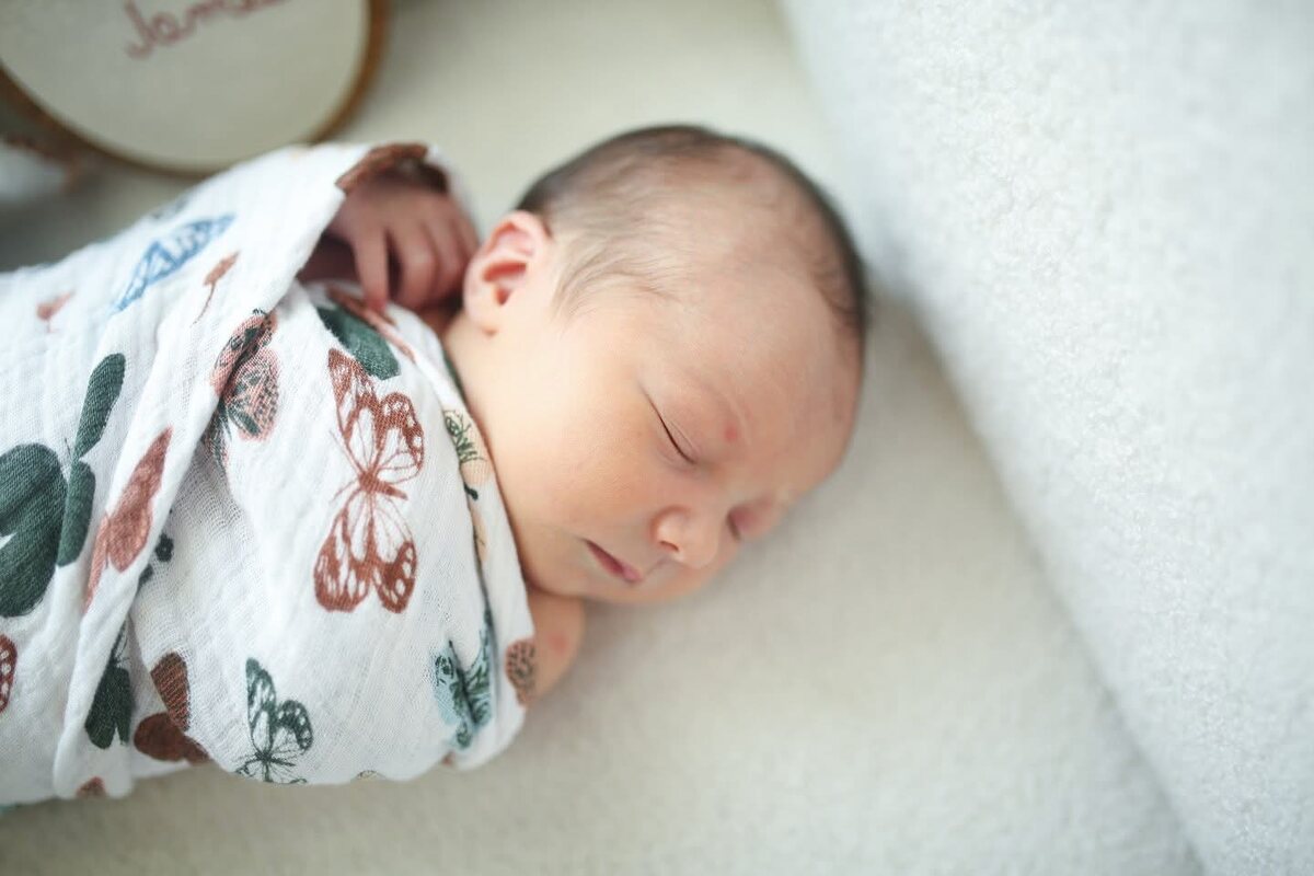 A newborn sleeping in a butterfly-print muslin swaddle