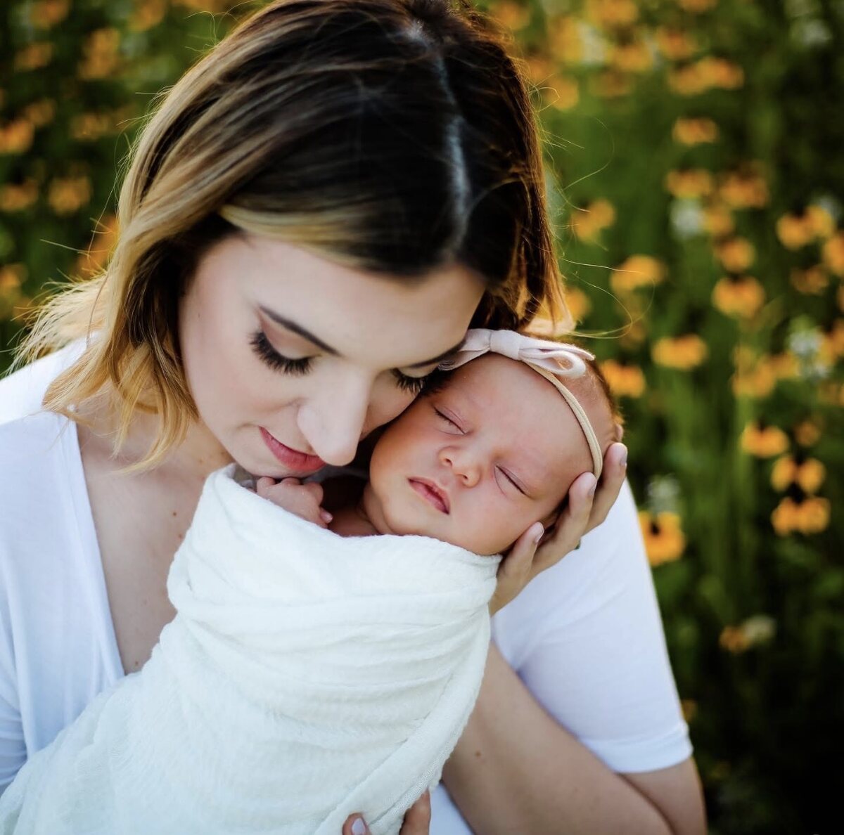A mother nuzzling her newborn daughter among yellow wildflowers