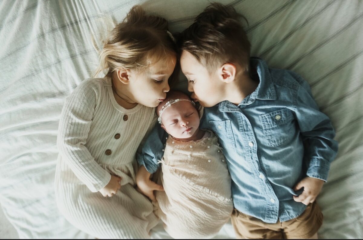 A big sister and big brother kissing their newborn sibling