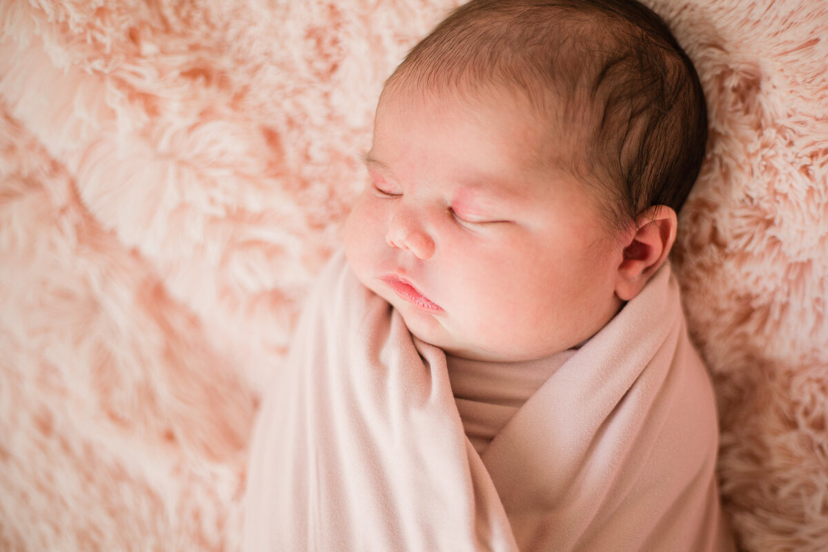 A newborn resting in a pink-trimmed swaddle on a white bed