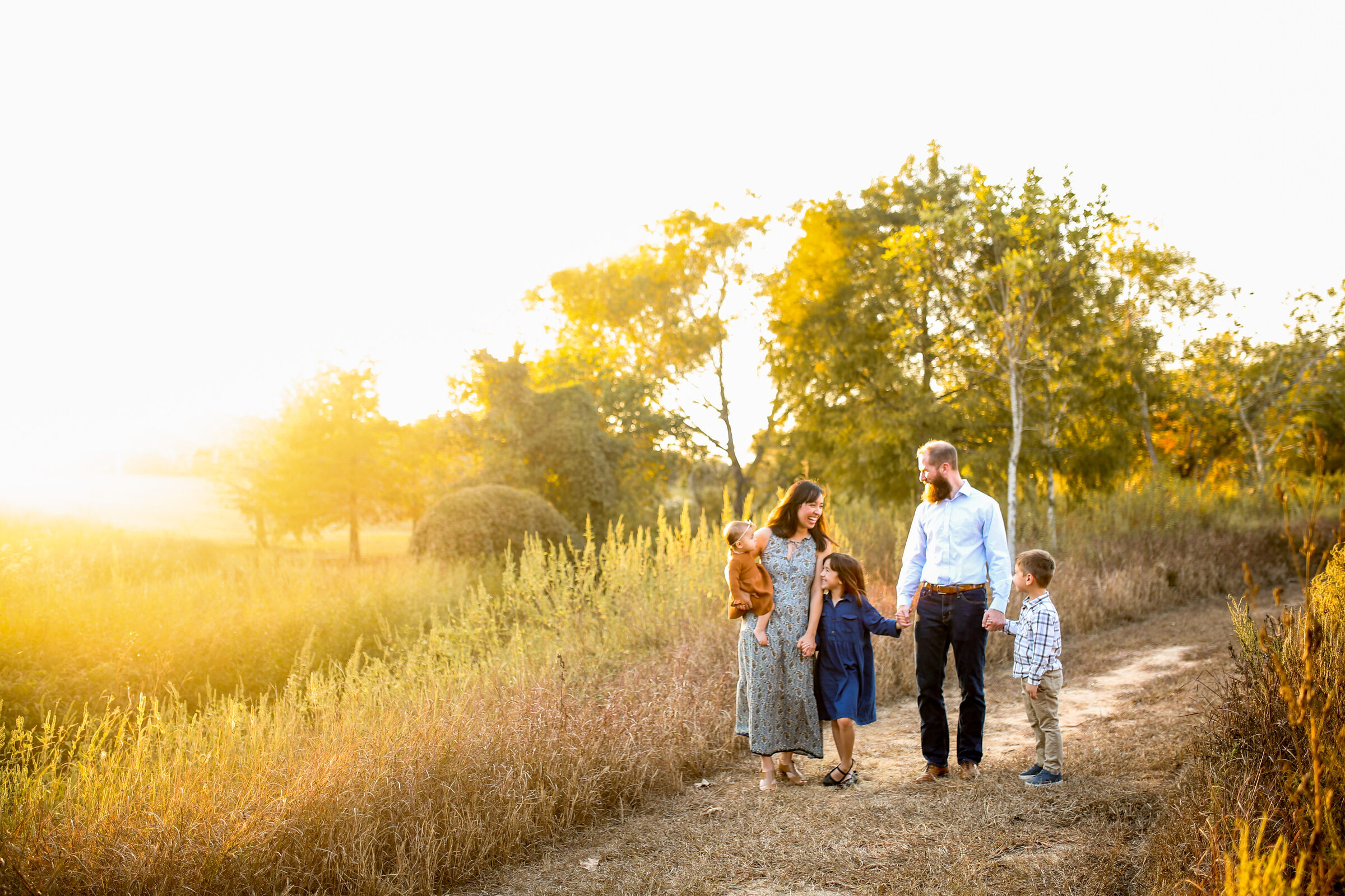 A family of five holding hands and laughing together on a golden country path at sunset
