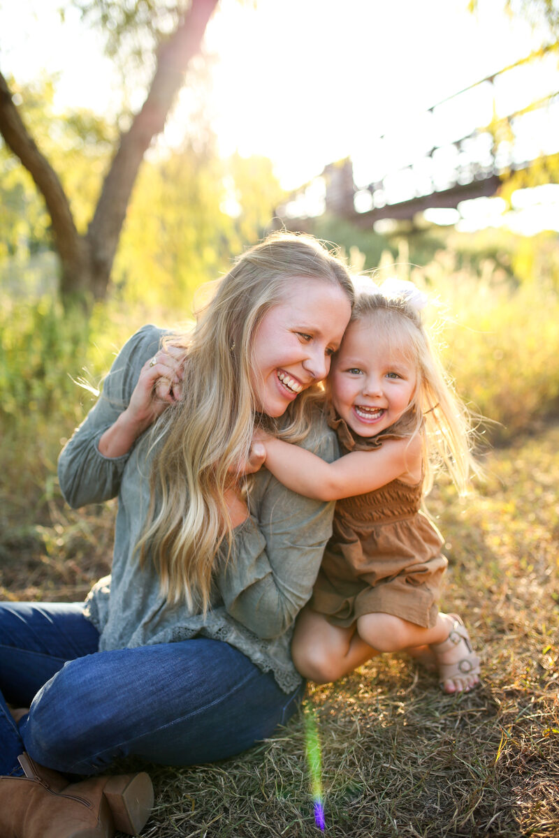 A mother and her young daughter laughing and hugging in golden evening light