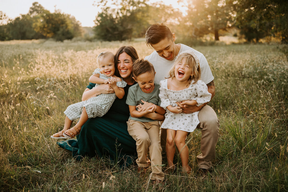 Nicole Whetzel laughing with her husband and three children in a golden field at sunset