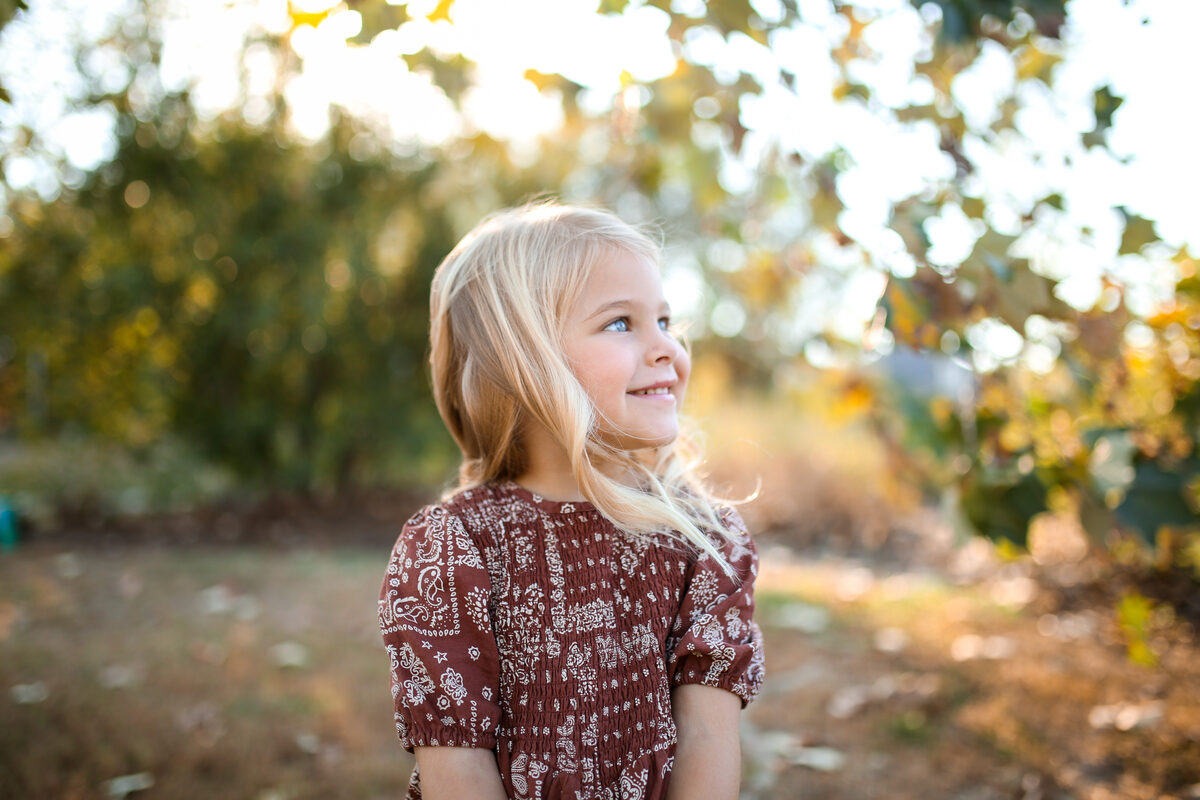 A young blonde girl in a paisley dress smiling in golden autumn light