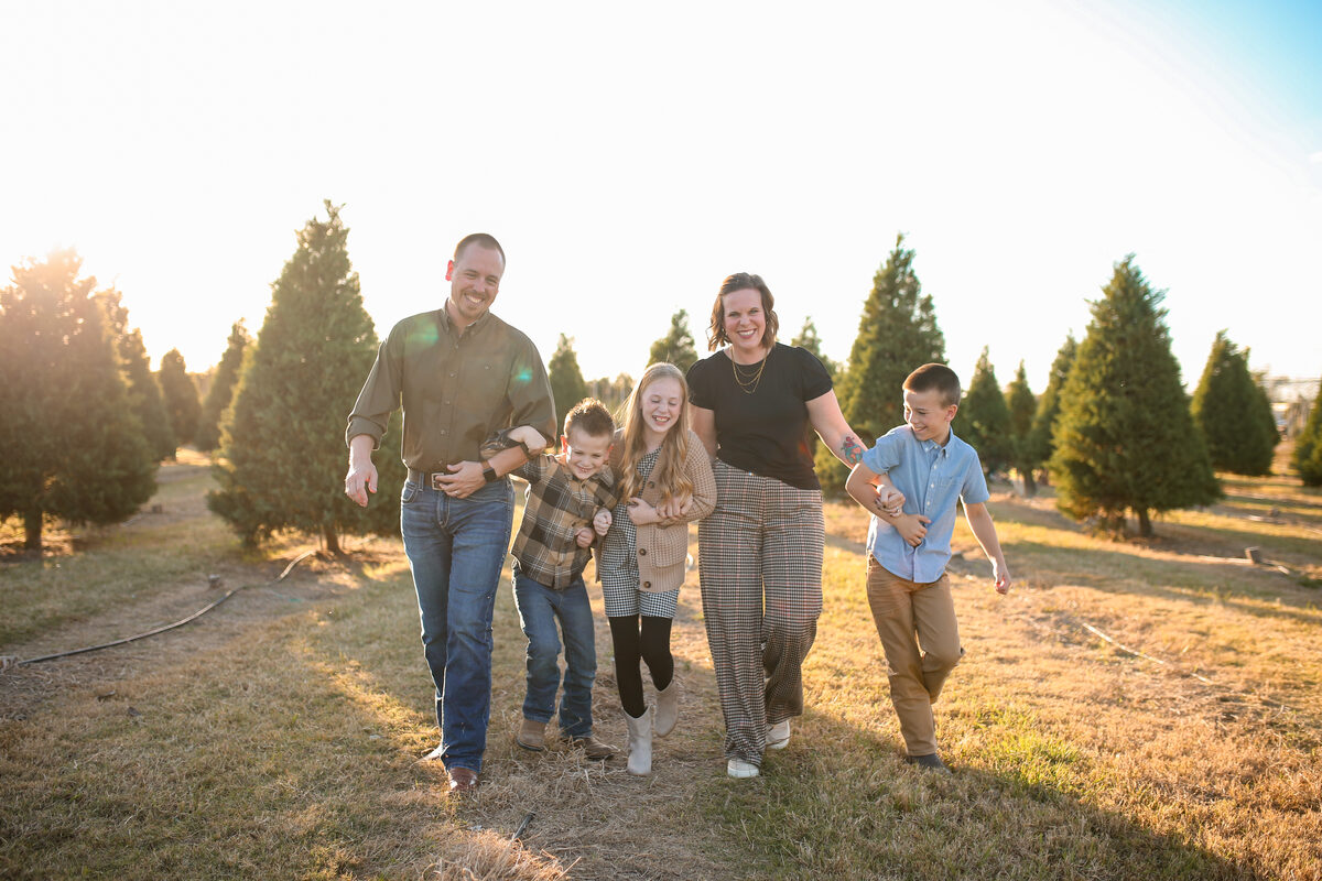 A family of five walking arm in arm through a Christmas tree farm at sunset
