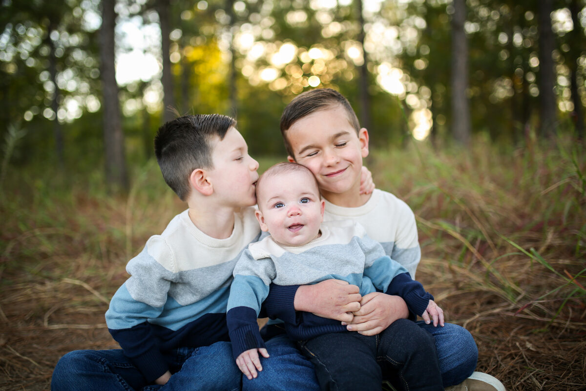 Three brothers snuggling their baby brother in a pine clearing