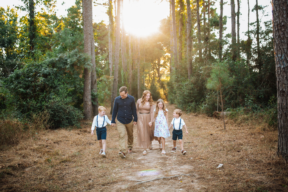 A family of five walking a sunlit pine path hand in hand