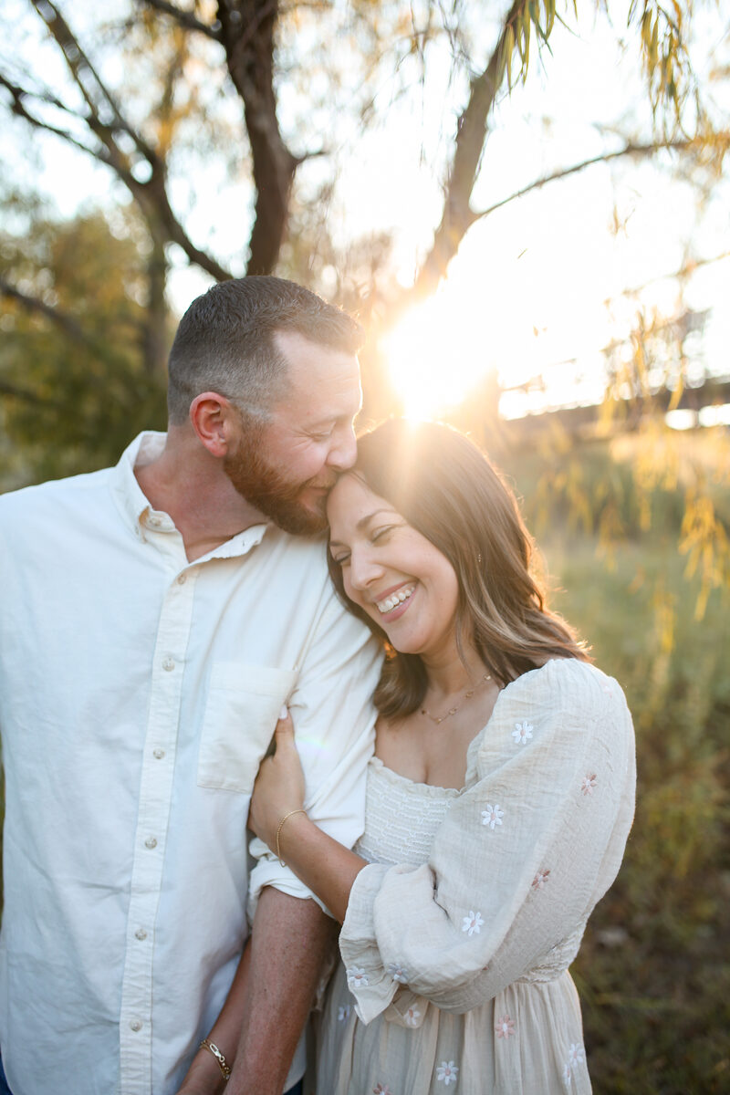 A husband kissing his wife's forehead in warm evening light