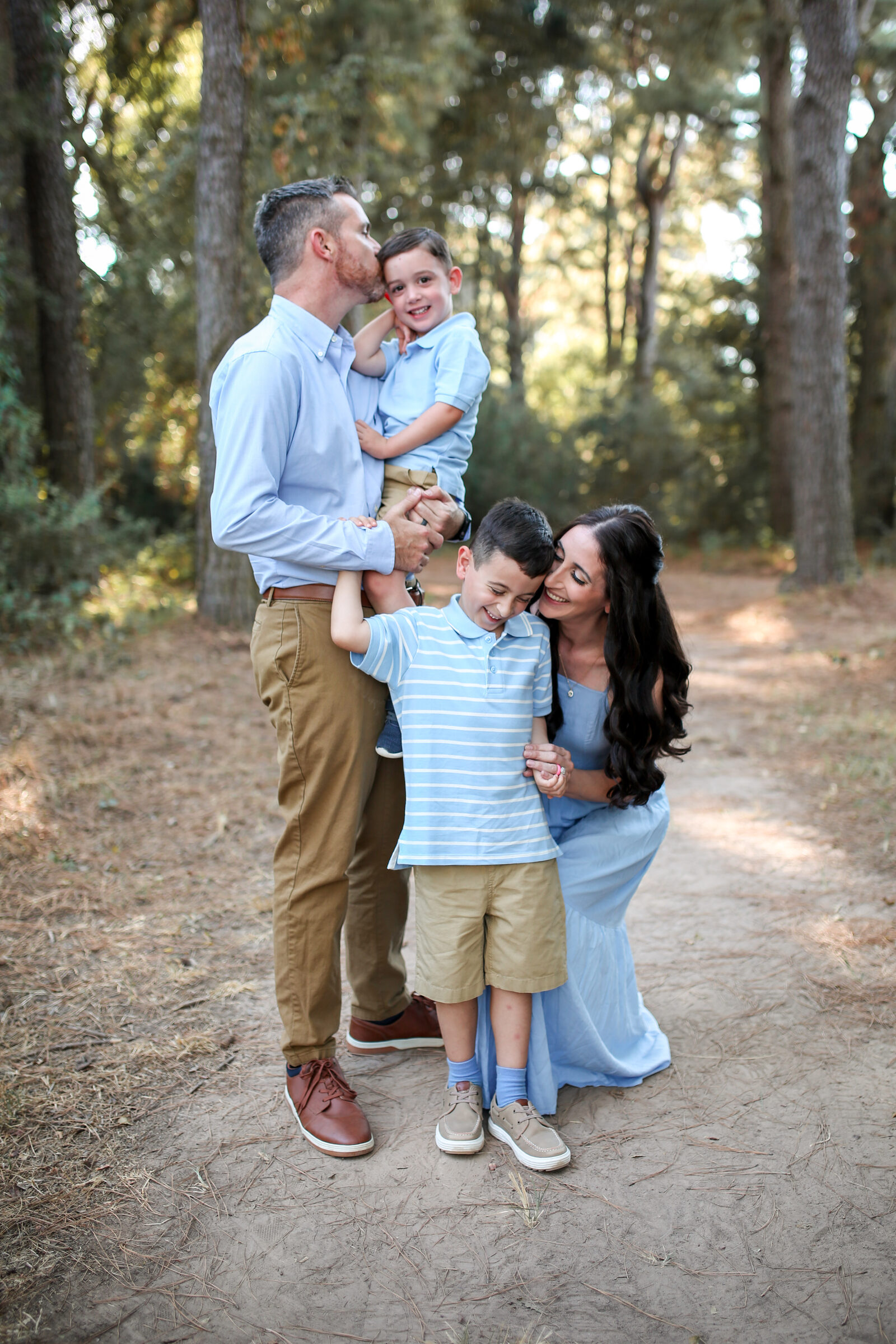 A mother and father snuggling their two boys on a sunlit pine trail