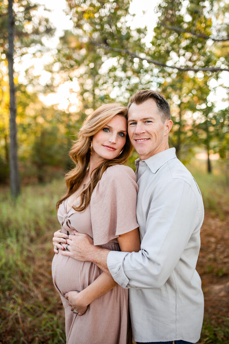 An expecting couple embracing in a sunlit autumn field