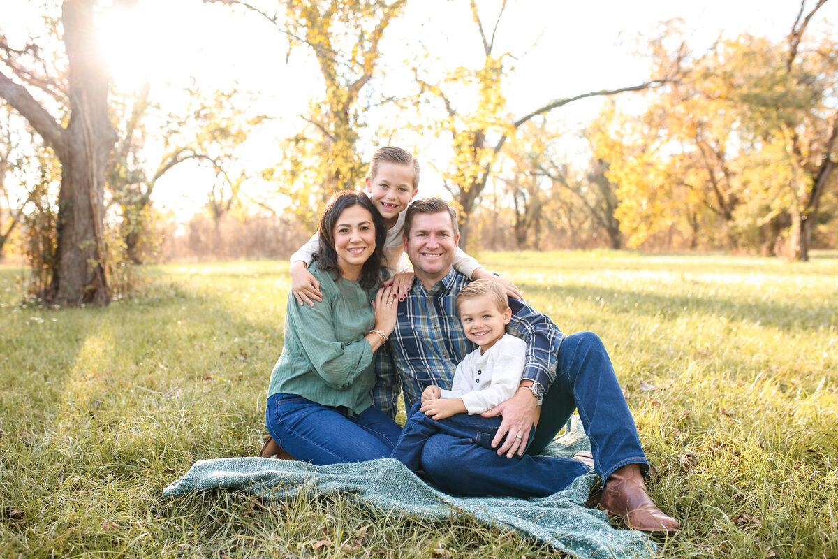 A family of four cuddled on a blanket in golden autumn light