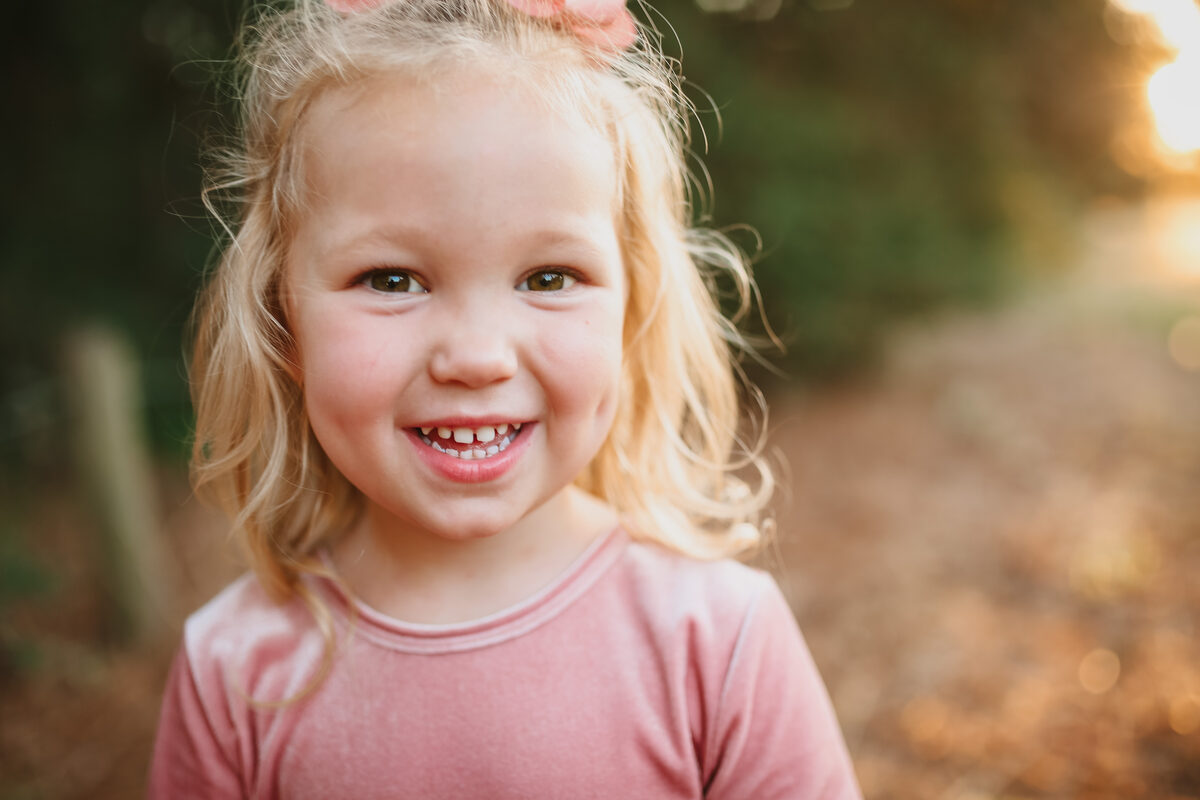 A little girl in pink smiling big at golden hour