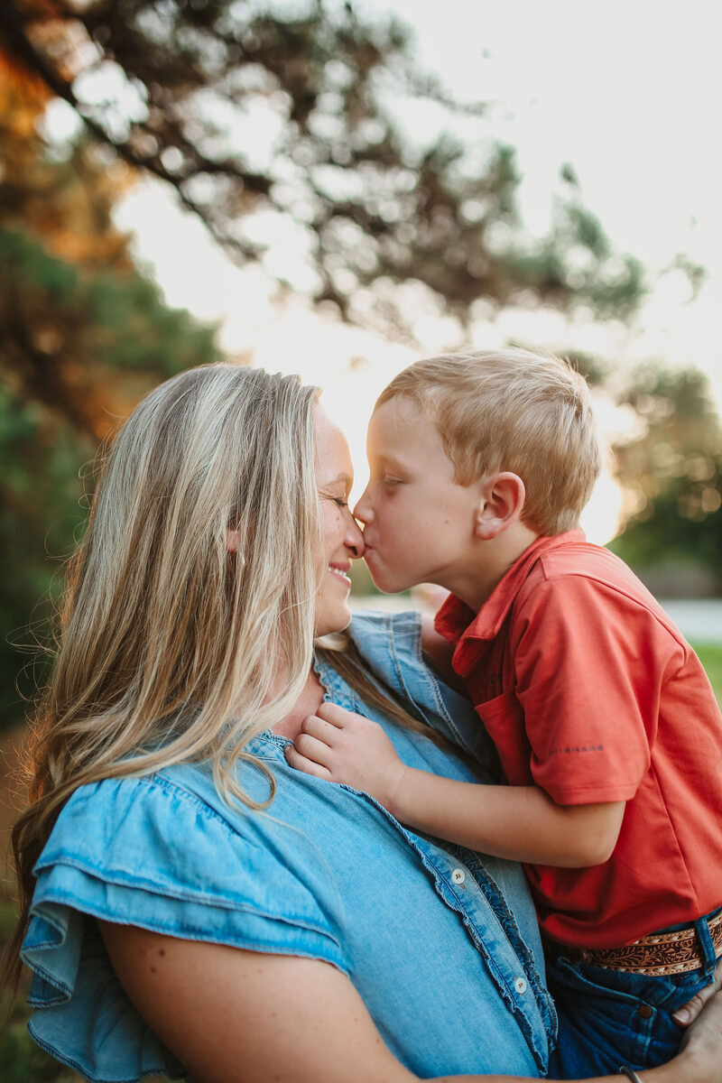 A young boy kissing his mother's nose at sunset