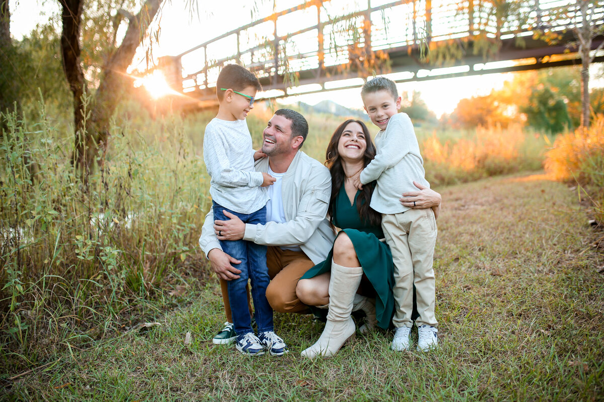 A family of four laughing together beneath a bridge at sunset