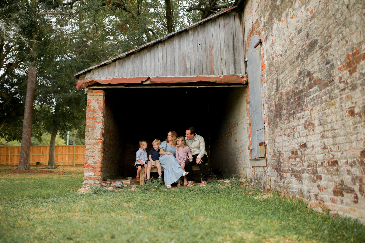 A family of five snuggled together on a bench inside a rustic brick barn