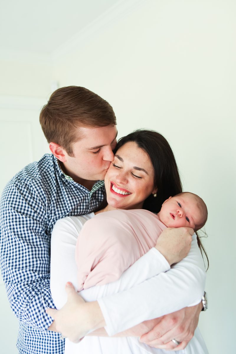 A father kissing mama's cheek while she snuggles their newborn
