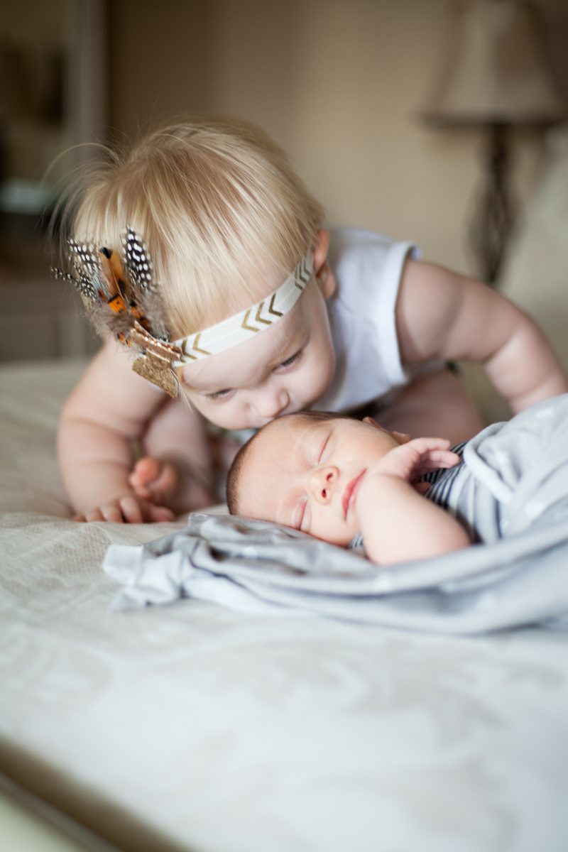 A toddler sister leaning in to kiss her newborn sibling